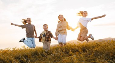 Neşeli bir grup okul çocuğu güneşli bahar gününde el ele zıplıyor, heyecanlı çocuklar ve kızlar yaz tatilinin tadını çıkarıyorlar.