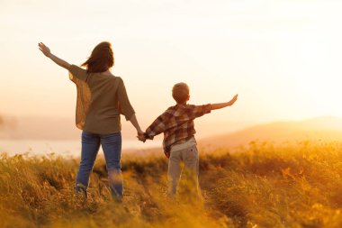 Mutlu aile anne ve oğlu gün batımında doğada yürüyor.