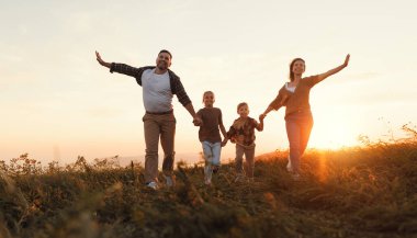 Mutlu aile: anne, baba, çocuklar gün batımında doğada koşan oğul ve kız