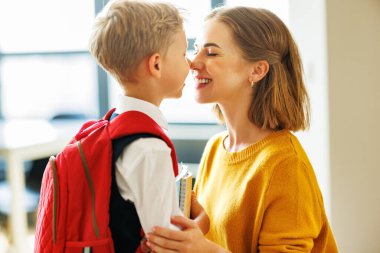 Okuldaki ilk günüm. Anne, evde okul eğitimi için hazırlanırken evrak çantasını mutlu oğluna ayarlar.