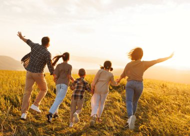 Mutlu aile: anne, baba, çocuklar gün batımında doğada koşan oğul ve kız