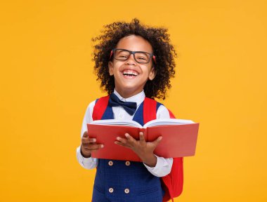 Gözlüklü, kameraya gülümseyen ve kitap okuyan Afro-Amerikan çocuk okul öğrencileri sarı arka planda eğlenirken.