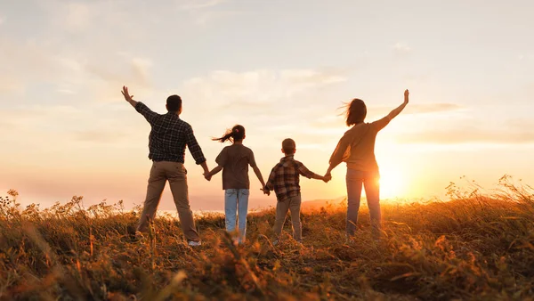 Mutlu aile: anne, baba, çocuk, oğul ve kız gün batımında doğanın arkasında durur.