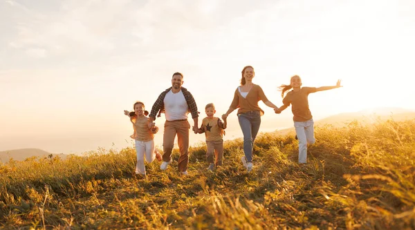 stock image Happy young parents with children in casual clothes running with holding hands while enjoying time together on meadow in summer evening