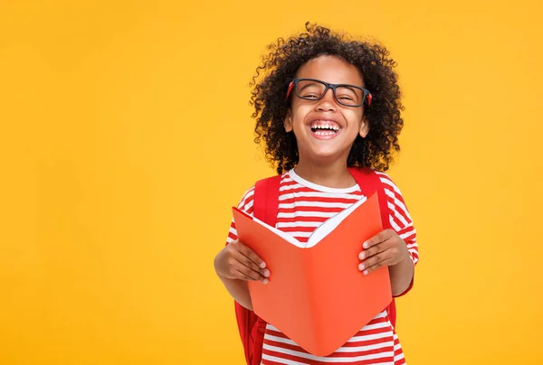 黄色い背景の学生の間楽しんでしながら カメラと読書本のために笑う眼鏡の光栄なアフリカ系アメリカ人の少年 — ストック写真