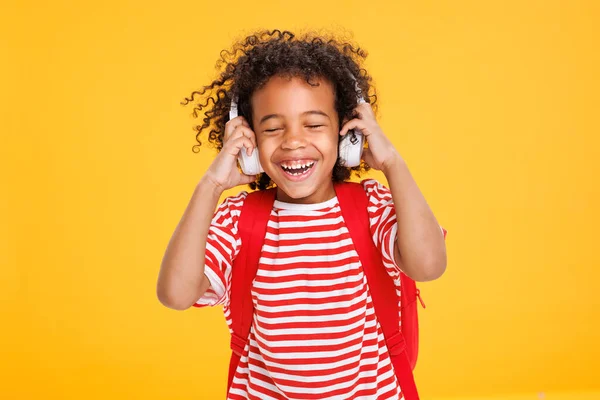 ストライプTシャツでアフリカ系アメリカ人の笑う少年は 黄色の背景に対する学校の研究の後に音楽を聞いている間 ヘッドフォンを調整 — ストック写真