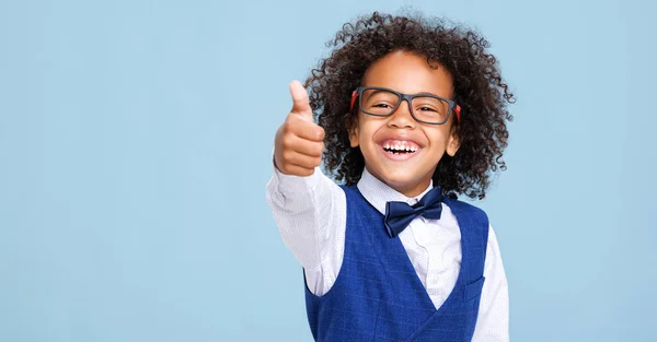 ポジティブなスマートなアフリカ系アメリカ人の少年は カメラのために微笑み 青色の背景に対する学校の研究中に親指を振る — ストック写真