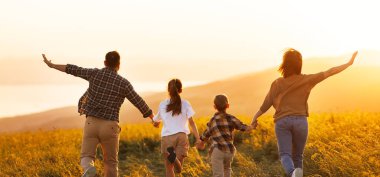 Mutlu aile: anne, baba, çocuk, oğul ve kız gün batımında doğaya koşuyorlar.