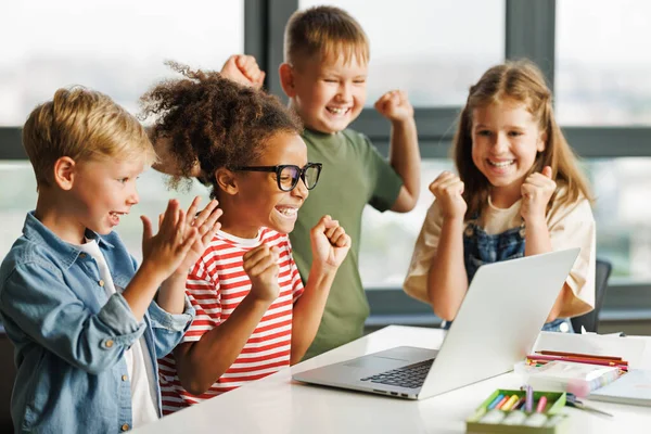 ポジティブな子供たちは 子供たちが笑顔で笑顔でラップトップスクリーンを見ながら ライト教室での集団学校の仕事の成功を祝います — ストック写真