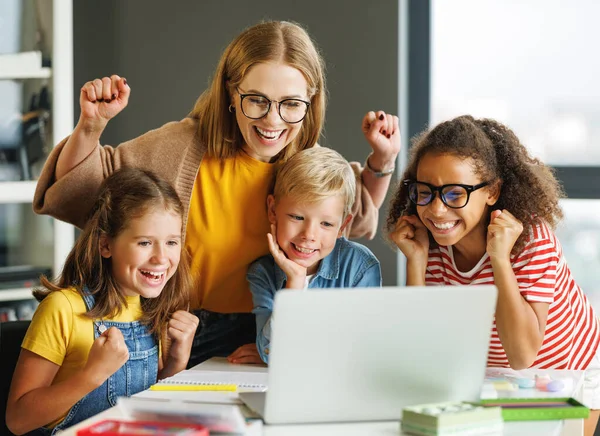 幸せな女性のチューターと学校の子供たちのグループ笑顔とラップトップスクリーンを見ながら一緒にライト教室での集団学校の仕事の成功を祝う — ストック写真