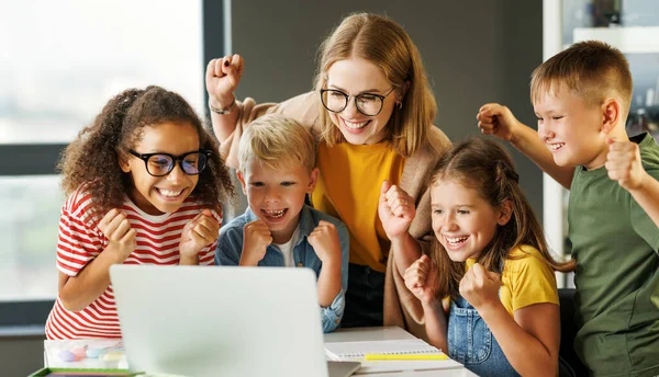 幸せな女性のチューターと学校の子供たちのグループ笑顔とラップトップスクリーンを見ながら一緒にライト教室での集団学校の仕事の成功を祝う — ストック写真