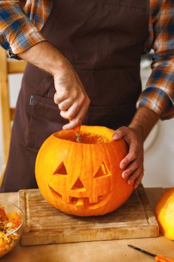 Cadılar Bayramı partisi için mutfakta dikilen önlüklü bir adam ve büyük turuncu bir balkabağı oyurken şaka mı şeker mi oynayanların havasına girmek için bıçaklı korkunç bir yüz ifadesi takınıyordu. 
