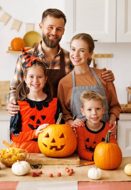 Mutlu aile anne, baba ve çocuklar karnaval kostümleriyle kameraya bakarken, balkabağından balkabağı kabağı yapıp cadılar bayramı için hazırlanıyorlar.