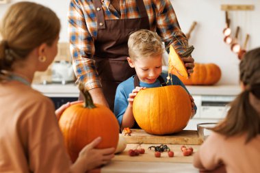 Mutlu çocuk bir yandan gülümserken bir yandan da babasına balkabağı oymasında yardım ediyor. Neşeli bir aile Cadılar Bayramı 'na hazırlanıyor. Bir balkabağı feneri oyarak.