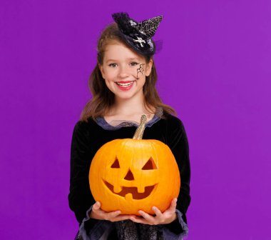 Cadılar Bayramı 'nı balkabağı kabaklı neşeli kız kutluyor ve parlak mor arka planda gülüyor.