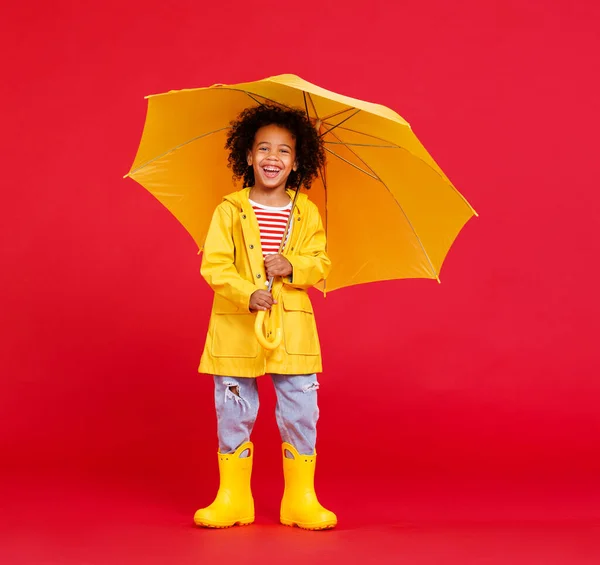 雨の日に赤い背景に向かって歩いている間 傘を持って立っている面白いアフリカ系アメリカ人の少年 — ストック写真