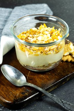 Bardakta puding ya da cheesecake tatlısı, lezzetli ve sade, bisküvi ve kremayla ahşap kesim tahtasında.