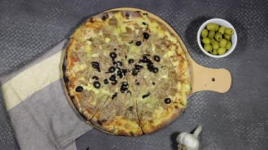 Yakın plan eller peynirli, domatesli ve zeytinli ton balıklı pizza tutuyor.