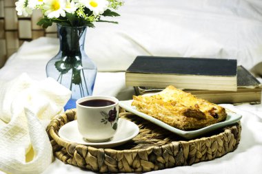 Kahvaltı tepsisi: Ev yapımı pofuduk elmalı tart, dondurmalı ve papatya çiçekli ve otel odasında kitaplarla birlikte bir fincan kahve. 