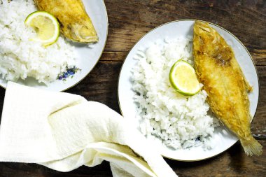 Tahta masada beyaz tabakta pilavlı ev yapımı kızarmış balık limonu.