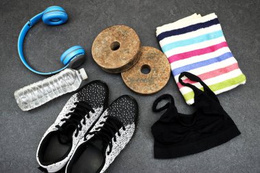 Healthy lifestyle, sport or athlete's equipment set : man or woman clothing and bottle of water with blue wireless headphone and dumbbell, sneakers and towel on gray background