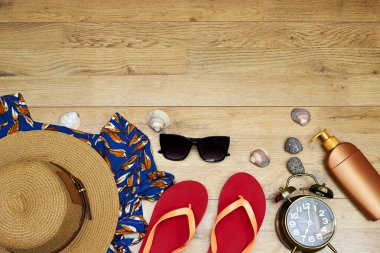 Elveda ya da merhaba yaz konsepti, güneş gözlüğü ve şapka, güneş kremi ve terlik ve büyük elbise ve çalar saat ahşap masa üzerinde