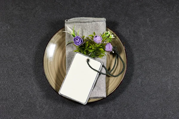 Festive fashion table setting. On the plate is a personal invitation with empty tag and flowers. The distribution of guests in places at the festive table
