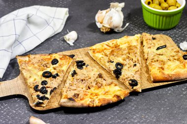 Peynirli, domatesli, zeytinli ton balıklı pizza yeşil zeytin kasesi ve sarımsaklı tahta kesim.