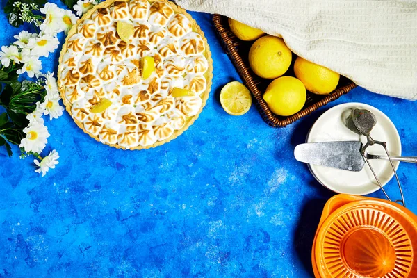 Traditional french lemon Meringue tart with fruits and orange juicer with daisy flowers  on blue grunge  background