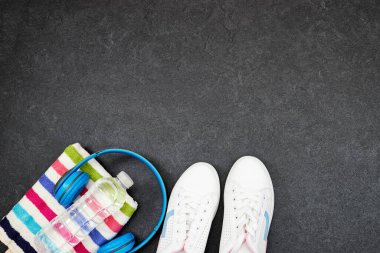 Sağlıklı yaşam tarzı, spor veya atlet ekipmanları seti: mavi kablosuz kulaklık ve havluyla bir şişe su, gri arka planda spor ayakkabıları