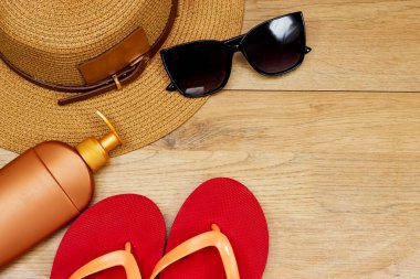 Yaz konsepti, güneş gözlüğü ve şapka, ahşap masada güneş kremi ve terlik.