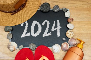 Yaz konsepti, güneş kremi ve terlik 2024 ile karatahta ve taşlarda. Ahşap masada deniz kabuğu