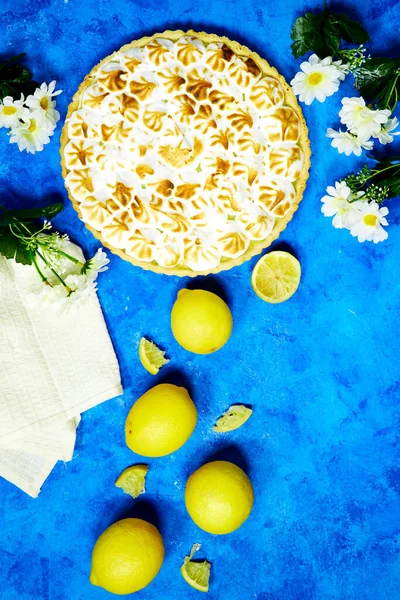 Traditional french lemon Meringue tart with lemon fruits with daisy flowers on blue grunge background