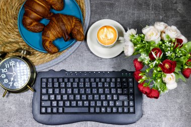 desktop - Fresh baked croissants on for breakfast and  coffee cup  and alarm clock showing seven o'clock  and keyboard on gray grunge background