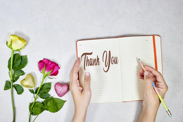 女人的手在写着谢谢你的文字 写在议程上或笔记本上 靠近玫瑰 鲜花和心灵闪耀 — 图库照片
