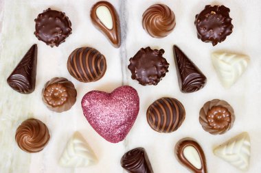 Sevgililer Günü için çeşitli kutulardan çikolata parçaları ve mermer arka planda küçük parlak bir kalp.