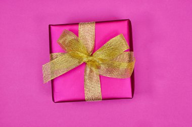 Pembe arka planda altın kurdeleli pembe hediye kutusu. düz yat