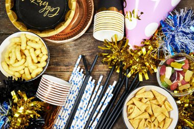Doğum günü ya da Noel, yeni yıl partisi konsepti, kartla kutlanan kağıt tabak metin ve tek kullanımlık kupa, pipet ve renkli farklı cips ve şekerler, ahşap masa üzerinde pembe şapka süslemesi