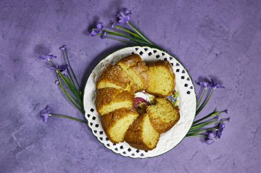Beyaz tabakta hindistan cevizli kek ve mor arka planda sardunya çiçekleri.