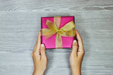Ahşap masaya altın kurdeleyle sarılı pembe bir hediye taşıyan kadın ellerini yakın çekim. tatil kavramı