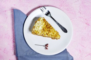 Cevizli kek ya da kremalı Kiev keki. Beyaz tabakta servis edilen vanilyalı tereyağı ve çingene çiçekleriyle süslenmiş pembe arka plan.