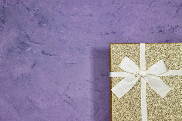 golden glitter gift box with golden ribbon on purple grunge wood background