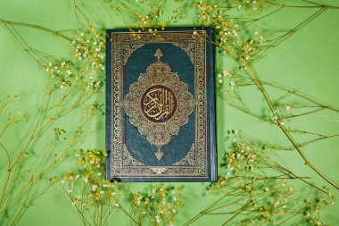 Arapça kaligrafi Kuran 'ı ile Müslümanların kutsal kitabı yeşil arka planda çigila çiçekleri.