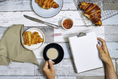 Kahvaltıda taze tatlı kruvasan ve portakal reçeli. Tahta masada kahvaltı, boş bir dosyayla el ele tutuşmak. Üst Manzara. Düz yatıyordu