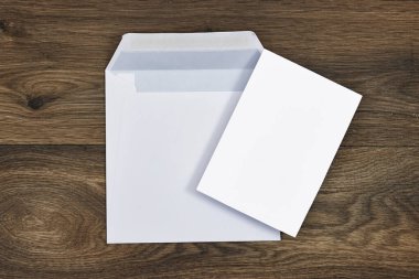 Düğün davetiyesi maketi ve ahşap masadaki beyaz zarf. Boş kart maketi