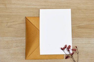 Boş tebrik kartı, el ilanı ya da davetiye kartı modeli, üzerinde çigila çiçekleri, ahşap masa üzerinde kahverengi el işi zarfı.
