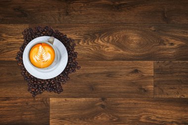 Sütlü kahvenin üstüne Latte 'nin güzel bir dokusu. Tahta sehpanın üzerinde kahve çekirdekleri olan yaprak ağacında süt köpüğü.