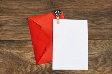 Düğün davetiyesi maketi ve ahşap masa üzerinde kalp şeklinde raptiye olan kırmızı kağıt zarf. Boş kart maketi