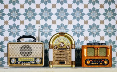 Üç farklı stil retro radyo çalar beyaz ahşap bir masanın üzerinde duruyor. Döşeme duvarının yanında