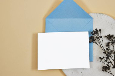 Üzerinde boş kağıt ve mermer kürsünün üzerinde siyah gypthe çiçekleri olan mavi zarf - bej arka planda beyaz kağıt levha